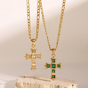 Gold cross necklaces with white and green stones on a stone pedestal for women