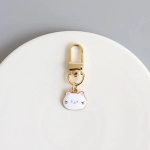Cute white enamel cat head keychain with gold metal clasp on a minimalist ceramic plate