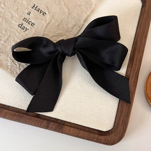 Detailed macro view of high-quality black satin bow hairclip on a beige display tray