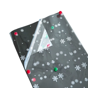 Black Christmas cellophane wrap with white snowflake pattern and festive pom pom accents