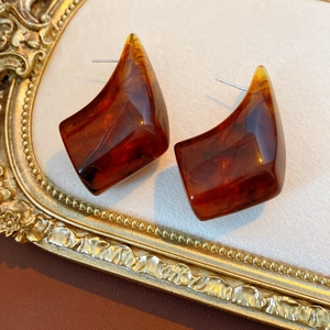 Close-up of amber resin geometric earrings on a vintage gold frame background