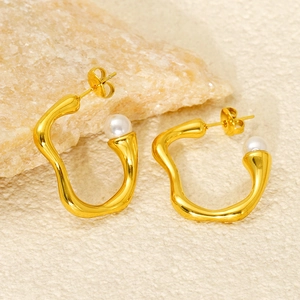 Gold irregular wave hoop earrings with white pearls on a minimalist stone display