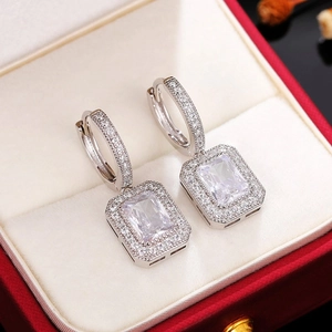 Detailed close-up of silver halo earrings with rectangle cut moissanite on red velvet box