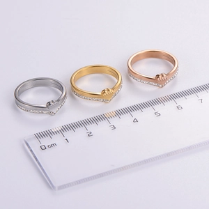 Three V-shaped heart diamond rings in silver, gold, and rose gold with a ruler