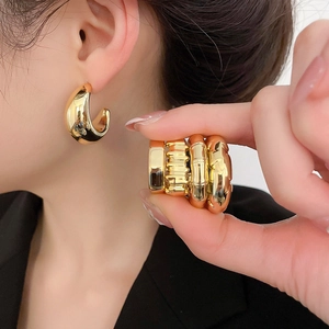 Close-up of polished gold-finish C-shaped earrings and textured metal bands on model
