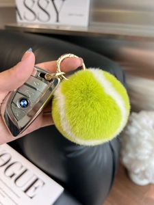 Close-up of fluffy faux rabbit fur tennis ball keychain on a luxury car key