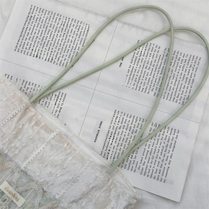 Close-up of elegant white lace tote bag with light green straps and gold metal tag