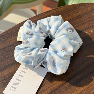 Detailed texture of blue checkered scrunchie featuring cute grey poodle prints and tags