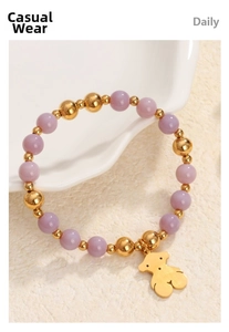 Macro detail of purple bead bracelet with gold bear charm on ceramic surface