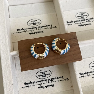 Détail macro de boucles d'oreilles créoles dorées avec émail rayé blanc et bleu