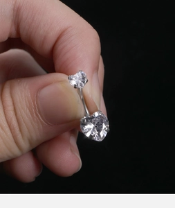 Macro shot of a heart-shaped zircon belly ring made of titanium steel held by fingers