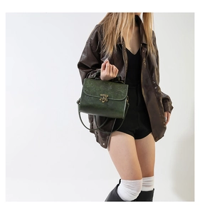 Detail of vintage green embossed crossbody bag with antique gold clasp on a model