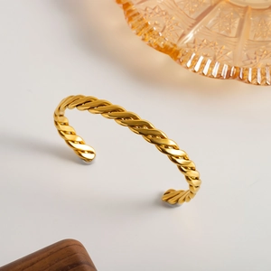 Detail shot of a minimalist 18K gold-plated twisted cable cuff bangle on decorative tray