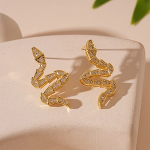 Macro shot of gold snake earrings with sparkling cubic zirconia on a stone surface