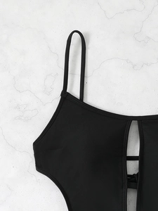 Detail of black cutout swimsuit with thin straps and elastic fabric on marble