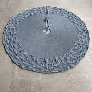 Detailed view of gray knitted Christmas tree skirt with decorative cable stitch patterns