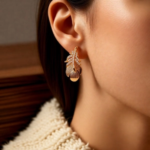Close-up of elegant 18k gold-plated feather earrings with pavé crystals on female model