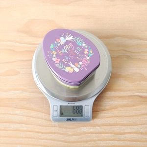 Flat purple Easter egg tin box with rabbit print being weighed on a digital kitchen scale