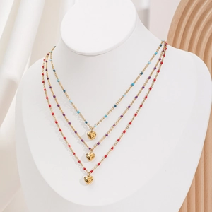 Détail de colliers superposés dorés avec des perles colorées et pendentifs en cœur