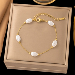 Detailed shot of golden stainless steel bracelet with five white oval beads and lobster clasp