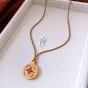 Close-up of vintage hollow gold pendant with ruby zircon inlay and brown braided cord