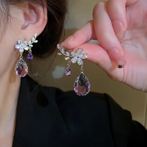 Detail of silver flower earring featuring zircon petals and a purple teardrop pendant