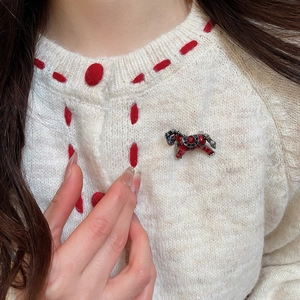 Gros plan d'une broche cheval en émail rouge avec zircons sur un gilet en maille blanc