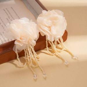 Detailed view of cream organza floral earrings with beaded tassels on wooden tray