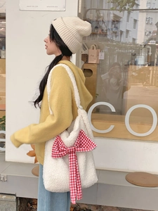 Close-up of a white plush tote bag featuring a large red and white checkered ribbon bow