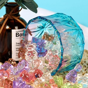 Close-up of colorful bear-shaped resin beads pouring from a blue geometric glass bowl
