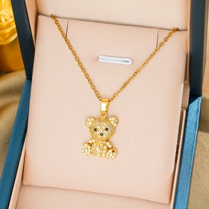 Detailed close-up of a golden teddy bear necklace with white rhinestones in a blue gift box