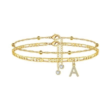 Detail of layered gold Figaro chains featuring a rhinestone letter A pendant and beads