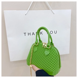 Detail of green PVC shell bag with golden metal handle and chain strap held by hand