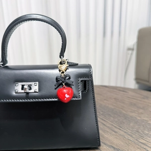 Detailed view of red heart bag charm with black bow and gold clasp on handbag