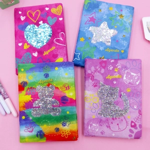 Flat lay of colorful plush sequin journals with Agenda text on soft pink background