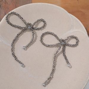 Detailed view of smoky gray crystal beaded bow earrings on a ceramic tray