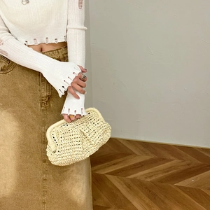 Beige straw woven clutch bag with chain strap carried by model in casual summer outfit