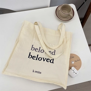 Close-up of cream canvas tote bag featuring beloved gradient lettering with lifestyle props