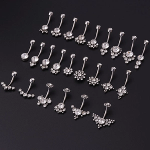 Various stainless steel belly rings with clear zircon crystals on a dark background