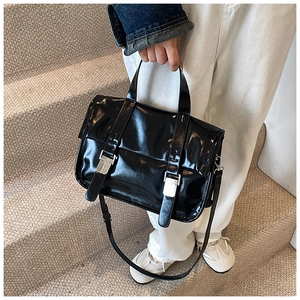 Detailed view of glossy black messenger bag with silver buckles in a street style setting