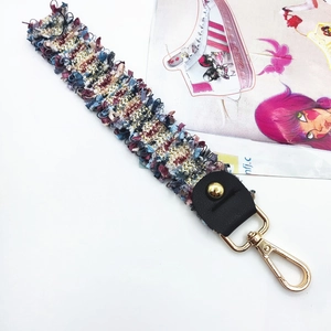 Close-up of colorful tweed woven bag strap with golden lobster clasp and fringe detail