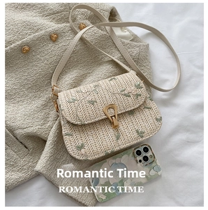 Detail of floral embroidery on beige straw shoulder bag with golden teardrop clasp
