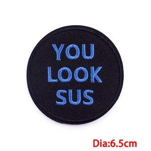 Détails de broderie de l'écusson rond avec texte bleu YOU LOOK SUS sur fond en tissu noir