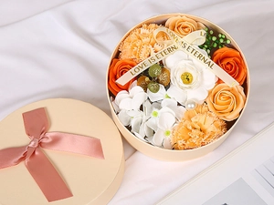 Close-up of round soap flower gift box with orange roses and LOVE IS ETERNAL ribbon