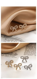 Detailed close-up of bow knot stud earrings with pavé rhinestones on satin fabric background