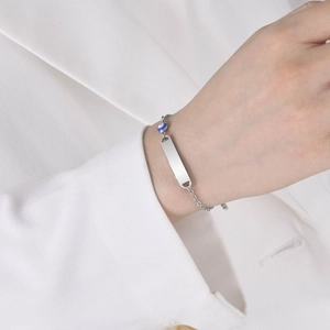 Close-up of a silver stainless steel chain bracelet with a blank bar and blue evil eye bead
