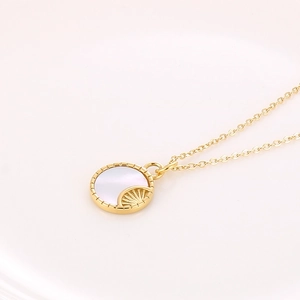Macro detail van gouden ketting met ronde witte schelphanger en zonnestraaltextuur