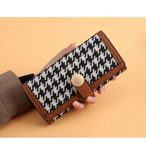 Detail of long houndstooth wallet featuring brown leather trim and snap button closure