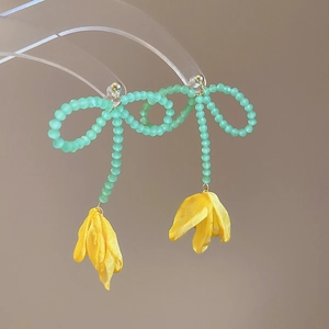 Dettaglio di orecchini a fiocco con perle verdi e nappine di petali di fiori gialli