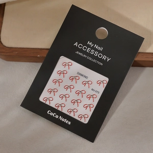 Close-up of 16-piece red bow nail charms with K9 rhinestones on black card packaging